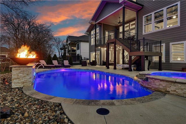 pool at dusk featuring an in ground hot tub, ceiling fan, an outdoor pool, a patio, and stairs