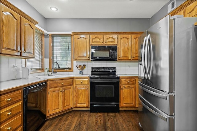 kitchen featuring dark wood-style flooring, light countertops, brown cabinets, a sink, and black appliances