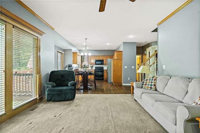 living area featuring stairs, dark carpet, baseboards, dark wood finished floors, and ceiling fan with notable chandelier