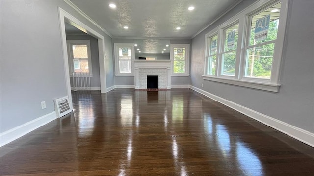 unfurnished living room with crown molding, a brick fireplace, baseboards, wood finished floors, and visible vents