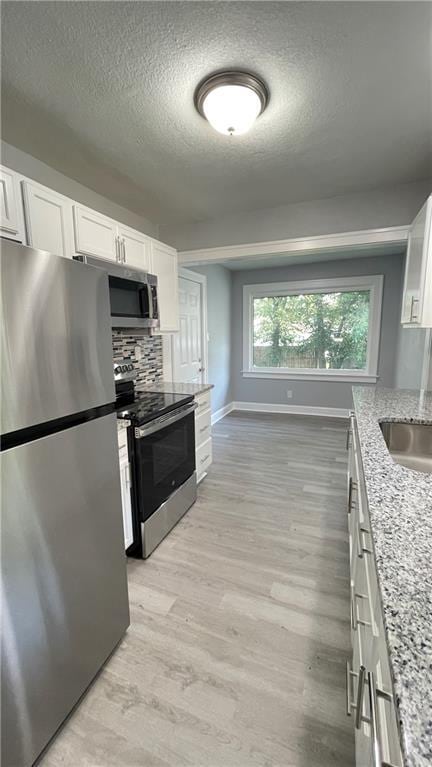 kitchen featuring a textured ceiling, appliances with stainless steel finishes, baseboards, white cabinets, and light wood finished floors