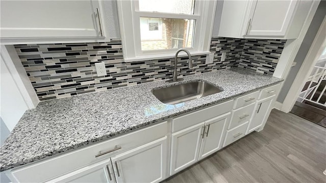 kitchen with decorative backsplash, light stone countertops, a sink, white cabinets, and light wood-style floors