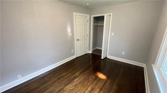 unfurnished bedroom with baseboards, dark wood-style floors, and a closet
