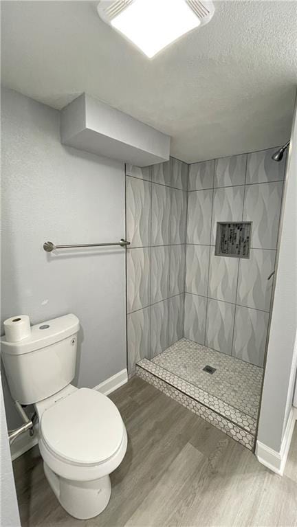 bathroom featuring baseboards, toilet, tiled shower, and wood finished floors
