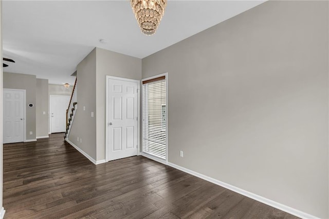 entryway featuring dark wood-type flooring, baseboards, a notable chandelier, and stairway