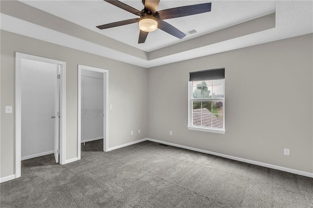 unfurnished bedroom with baseboards, a tray ceiling, dark colored carpet, and a spacious closet