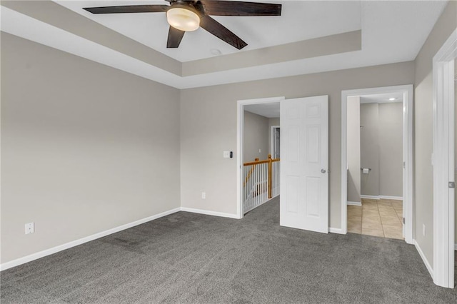 unfurnished bedroom featuring carpet floors, baseboards, and a raised ceiling