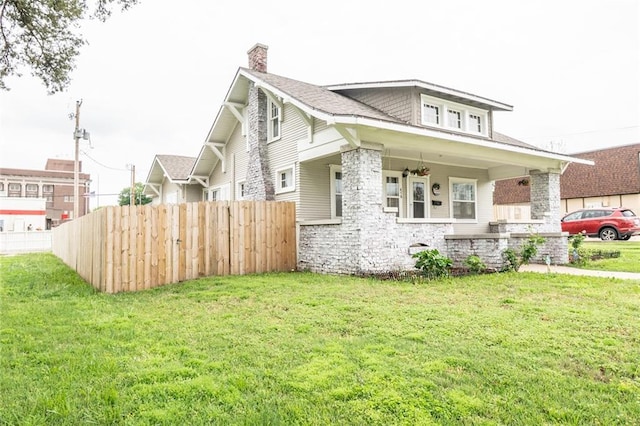 view of front facade with fence, a front lawn, stone siding, a porch, and a chimney
