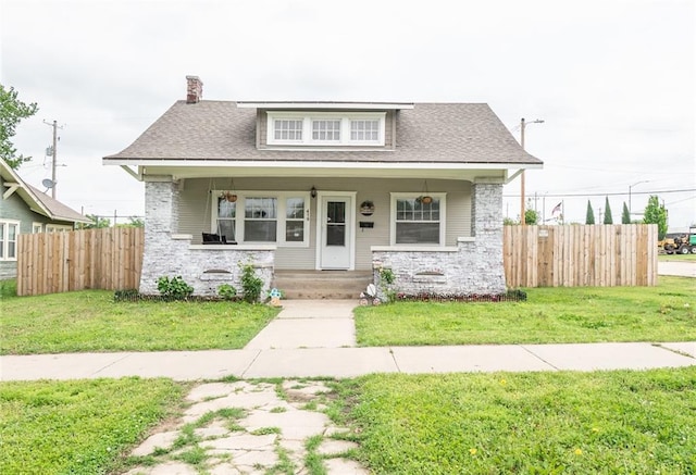 bungalow featuring fence, stone siding, and a front lawn