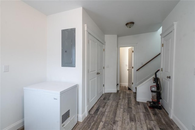 corridor featuring baseboards, electric panel, stairs, and wood finished floors