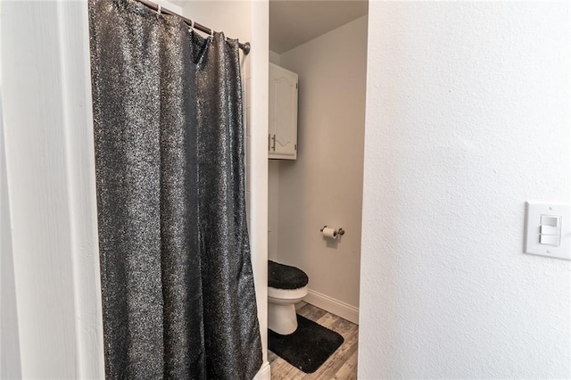 bathroom with toilet, baseboards, wood finished floors, and a shower with curtain