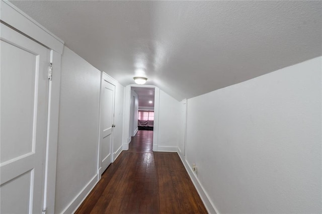 hall featuring baseboards, wood-type flooring, a textured ceiling, and lofted ceiling