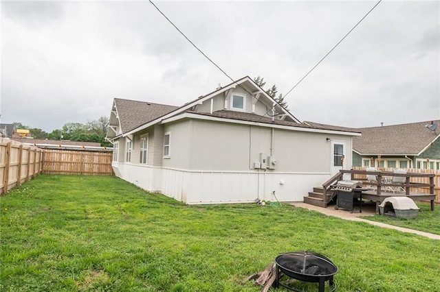 back of house featuring a lawn, a fenced backyard, a fire pit, and roof with shingles