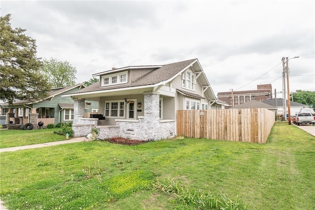 craftsman house with fence, roof with shingles, a front lawn, and stone siding