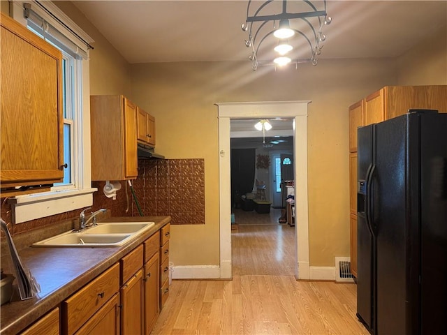 kitchen with black fridge, light wood-style floors, a sink, dark countertops, and baseboards