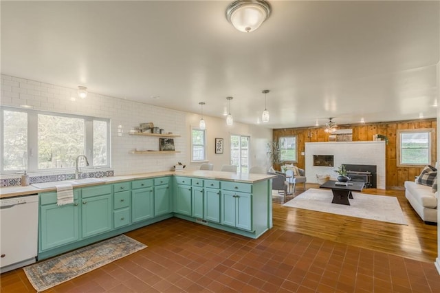 kitchen with a peninsula, white dishwasher, open floor plan, light countertops, and a sink