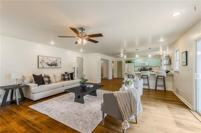 living room featuring a ceiling fan, baseboards, recessed lighting, and wood finished floors