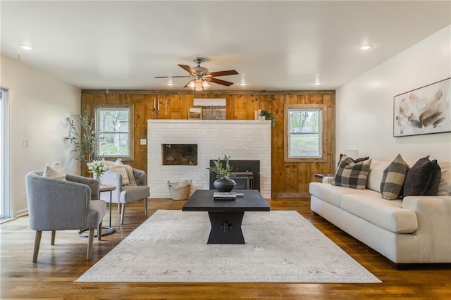 living area with wooden walls, a ceiling fan, wood finished floors, and a brick fireplace