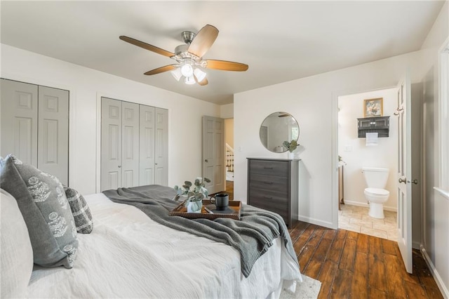 bedroom featuring a ceiling fan, baseboards, dark wood-style floors, multiple closets, and ensuite bath