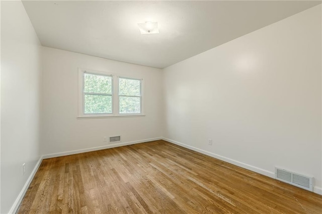 spare room featuring baseboards, wood finished floors, and visible vents