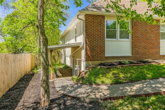 view of side of property featuring fence, roof with shingles, and brick siding