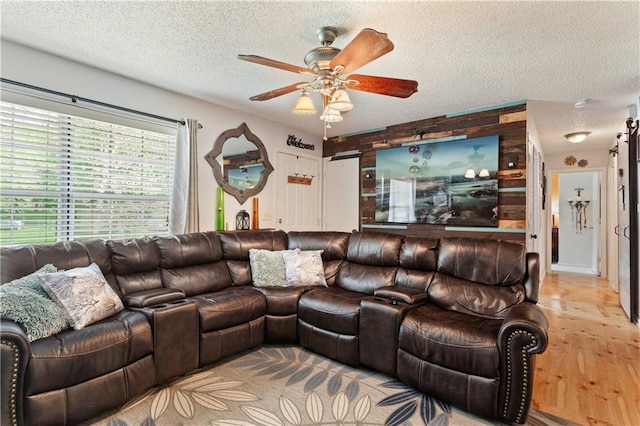 living area featuring a textured ceiling, wood walls, ceiling fan, and wood finished floors