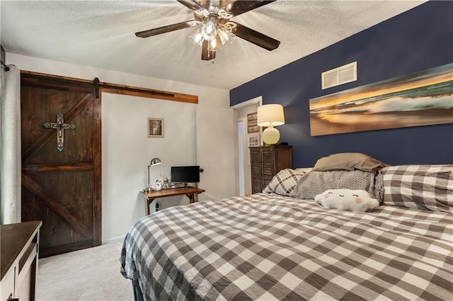 bedroom featuring ceiling fan, light colored carpet, a barn door, a textured ceiling, and visible vents