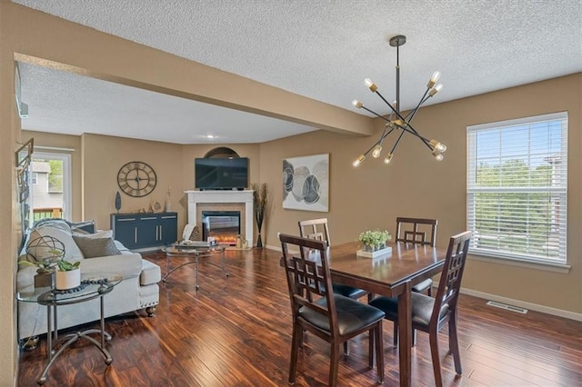 dining space with a textured ceiling, a glass covered fireplace, a chandelier, and hardwood / wood-style flooring