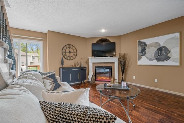 living room with a textured ceiling, baseboards, a tiled fireplace, and wood finished floors