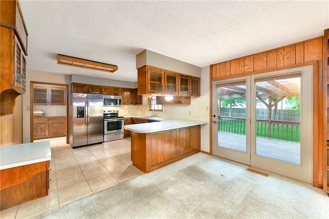 2217 Kingman St, Leavenworth, KS 66048 - kitchen with appliances with stainless steel finishes, a peninsula, light countertops, glass insert cabinets, and brown cabinetry