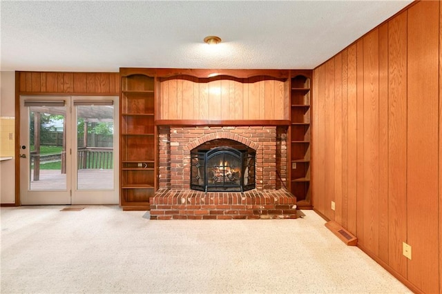 2217 Kingman St, Leavenworth, KS 66048 - unfurnished living room with wood walls, carpet flooring, a textured ceiling, a fireplace, and built in shelves
