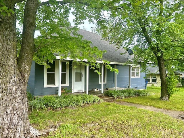 view of front of property featuring covered porch, roof with shingles, and a front lawn