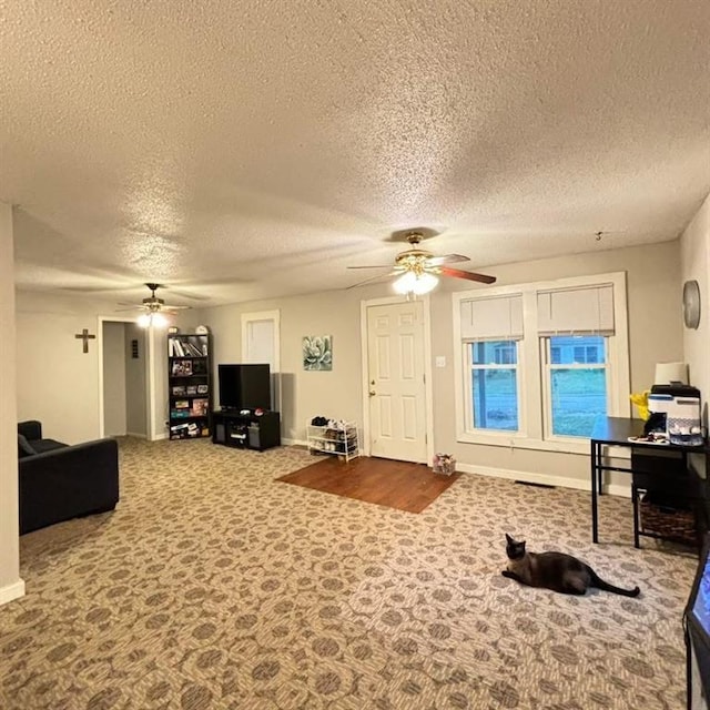 living room with baseboards, a textured ceiling, carpet, and ceiling fan