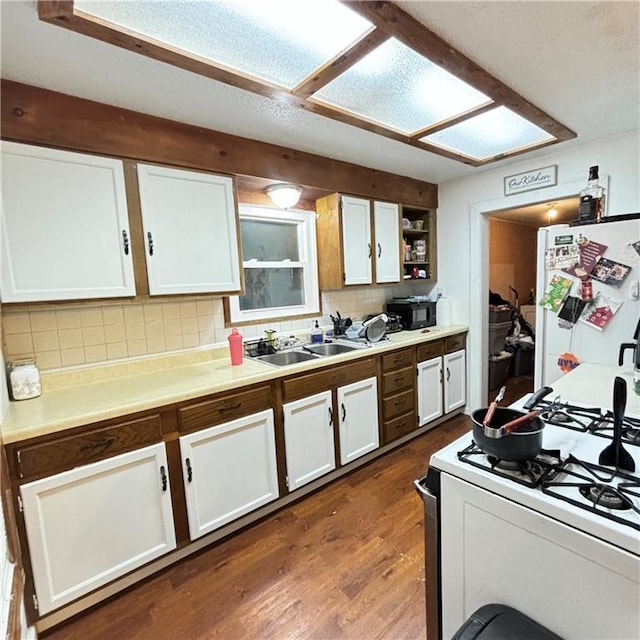 kitchen with white appliances, dark wood-type flooring, white cabinetry, a sink, and backsplash