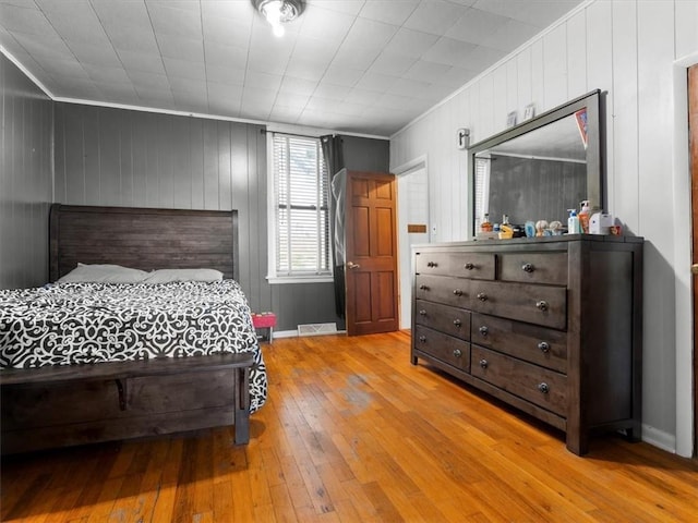 bedroom with light wood-type flooring, ornamental molding, and wooden walls