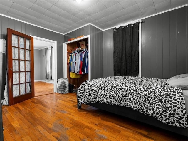 bedroom featuring ornamental molding, wood-type flooring, a closet, wood walls, and baseboards