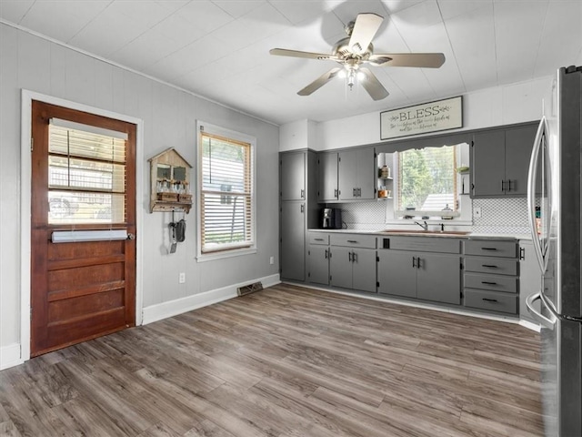 kitchen with gray cabinetry, freestanding refrigerator, decorative backsplash, wood finished floors, and ceiling fan