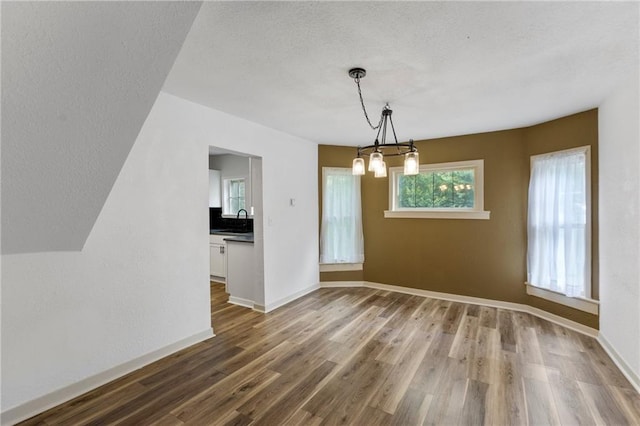 628 S Mulberry St, Ottawa, KS 66067 - unfurnished dining area with a chandelier, wood finished floors, baseboards, a textured ceiling, and a sink