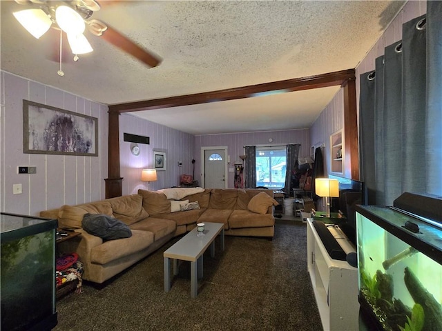 living room with a textured ceiling, ceiling fan, beam ceiling, and dark colored carpet
