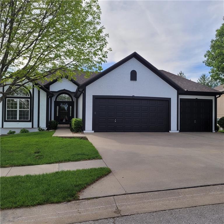 ranch-style home featuring stucco siding, driveway, a front yard, and a garage