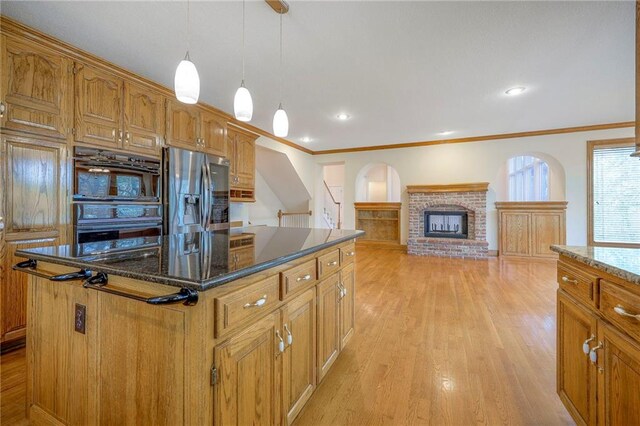 4411 N Mulberry Dr, Kansas City, MO 64116 - kitchen featuring dobule oven black, a brick fireplace, stainless steel fridge, light wood-type flooring, and a center island