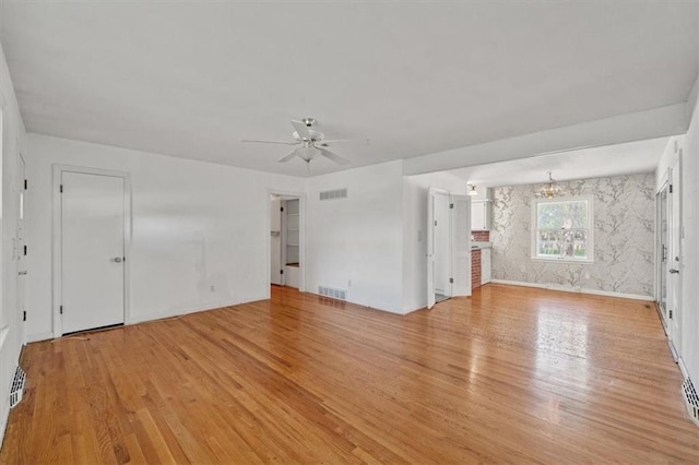 unfurnished living room featuring ceiling fan with notable chandelier, light wood-style flooring, and visible vents