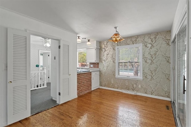 interior space with baseboards, light wood-style floors, a notable chandelier, and wallpapered walls