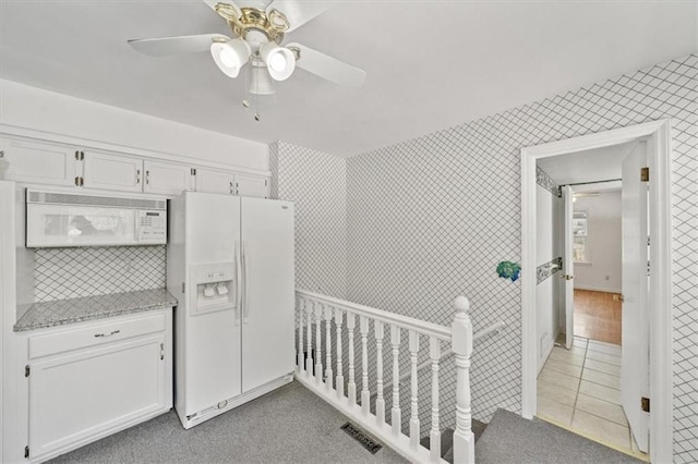 interior space featuring a ceiling fan, visible vents, tile walls, light tile patterned floors, and white fridge with ice dispenser