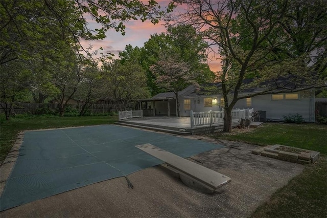pool at dusk featuring fence, a yard, and a deck