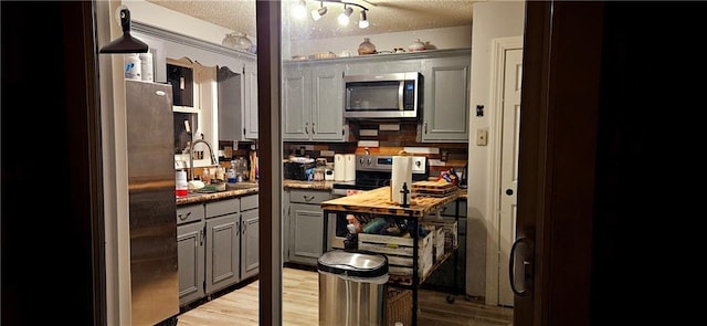 interior space with a textured ceiling, gray cabinetry, a sink, light wood-style floors, and stainless steel appliances