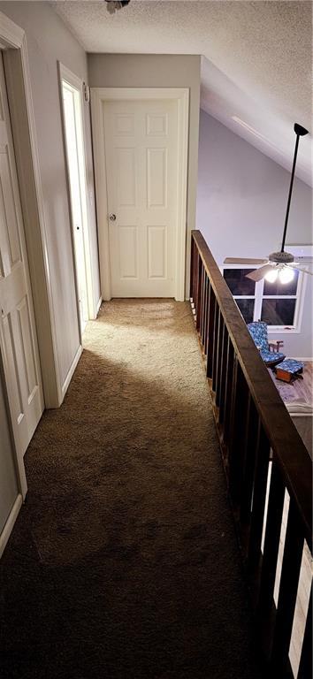 hallway with carpet floors, a textured ceiling, and vaulted ceiling