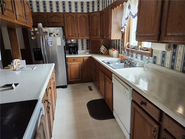 kitchen featuring white dishwasher, stainless steel fridge, a sink, light countertops, and wallpapered walls