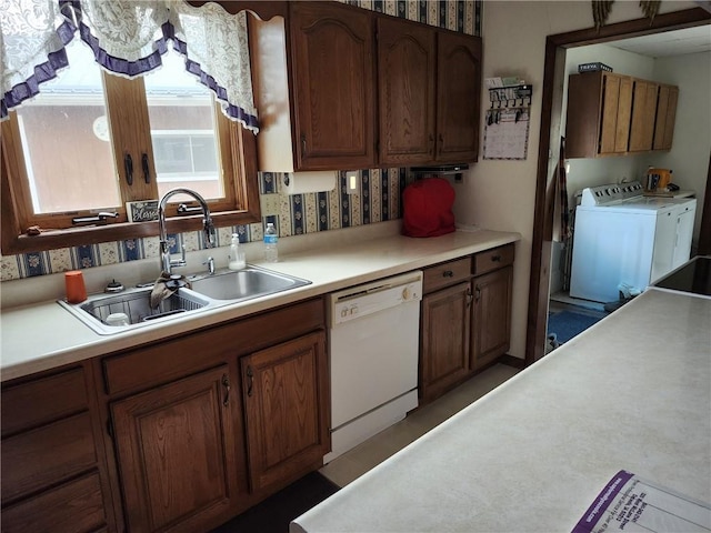 kitchen featuring brown cabinetry, washer and dryer, light countertops, a sink, and dishwasher