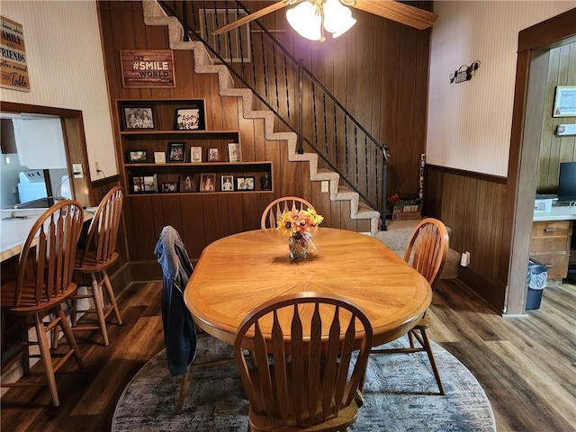 dining space featuring stairway, wood walls, wallpapered walls, and wood finished floors